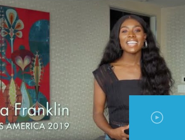 A woman with long, curly hair smiles while sitting indoors, embodying the essence of social emotional learning activities. She is wearing a black top, and a colorful abstract painting adds vibrancy to the scene. Text on the image reads "Franklin Miss America 2019.