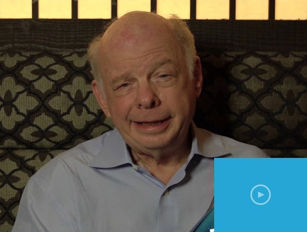 An older man with a receding hairline sits in a patterned chair, wearing a light blue shirt, surrounded by the soft glow of indoor light. The play button on this video thumbnail hints at insights into an SEL curriculum, inviting viewers to explore social emotional learning activities.