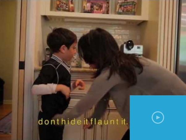 A woman crouches to adjust a young boy's clothing in the kitchen, fostering connection through social emotional learning activities. The boy, wearing a black shirt, looks curiously at her. The text "don't hide it flaunt it" is overlaid at the bottom.