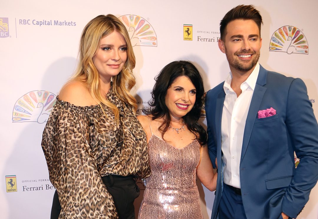 Group of two women and a man standing smiling on red carpet for awards