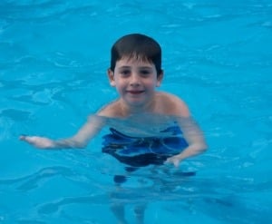 Ethan in pool A child swimming in a clear blue pool, engaging in social emotional learning activities, beams a smile at the camera.