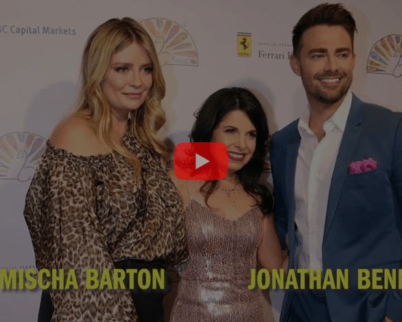 Three people pose together on a red carpet with event branding in the background, highlighting diversity programs. The two individuals on the sides have their names displayed at the bottom of the image. A play button overlay suggests this is a video thumbnail.