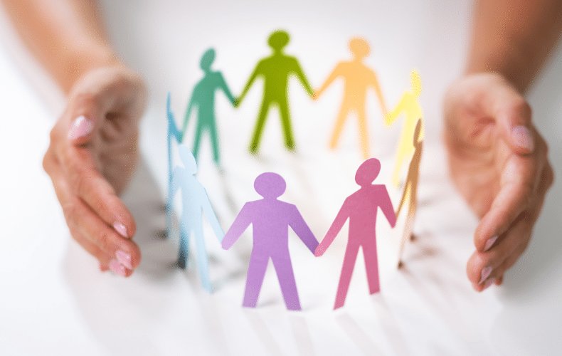 Hands encircle colorful paper cutouts of people holding hands, symbolizing unity and diversity, much like SEL activities promoting social emotional growth. The figures in blue, green, yellow, red, and purple form a circle on a white background.