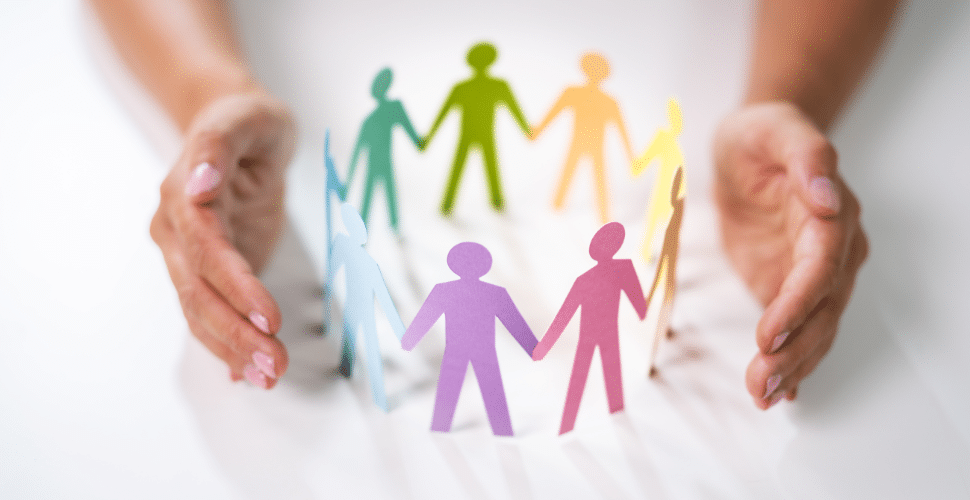 Hands encircle colorful paper cutouts of people holding hands, symbolizing unity and diversity, much like SEL activities promoting social emotional growth. The figures in blue, green, yellow, red, and purple form a circle on a white background.