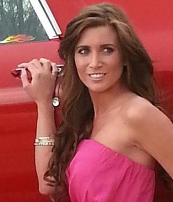 A woman with long, wavy hair in a strapless pink dress smiles beside a red car, her hand resting on the door handle where a flame decal glows. Her pose exudes confidence and positivity, much like the spirit embodied by social emotional learning activities.