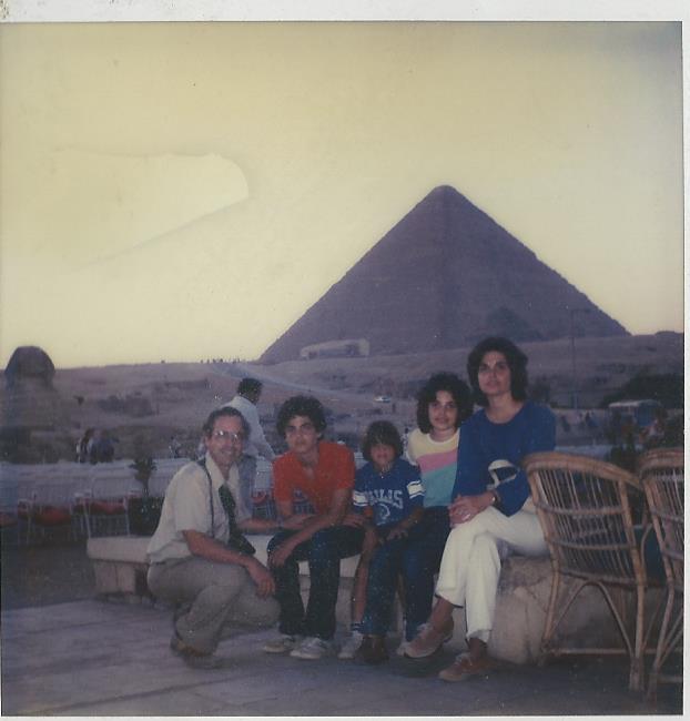 A family of five sits together on a bench, reflecting on their dynamic day filled with SEL activities, against the backdrop of the Great Pyramid and Sphinx of Giza. It's a sunny day with a clear sky.