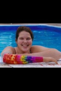 A person smiles at the camera while leaning on the edge of a swimming pool, their colorful tie-dye cast adding a splash of creativity. This vibrant display could be part of an SEL activity, encouraging students to express themselves in bold and unique ways.