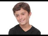 A child with short brown hair, smiling at the camera in a black shirt against a white background, embodies the joy and inclusivity fostered by diversity programs.