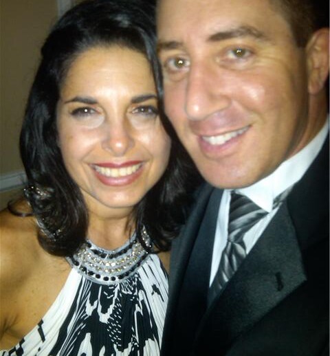 A woman and a man are smiling at the camera, exuding confidence. The woman, with long dark hair, dons a patterned dress with a jeweled neckline. The man sports a black suit and striped tie. They seem engaged in an event focused on SEL activities, promoting social emotional learning through connection.