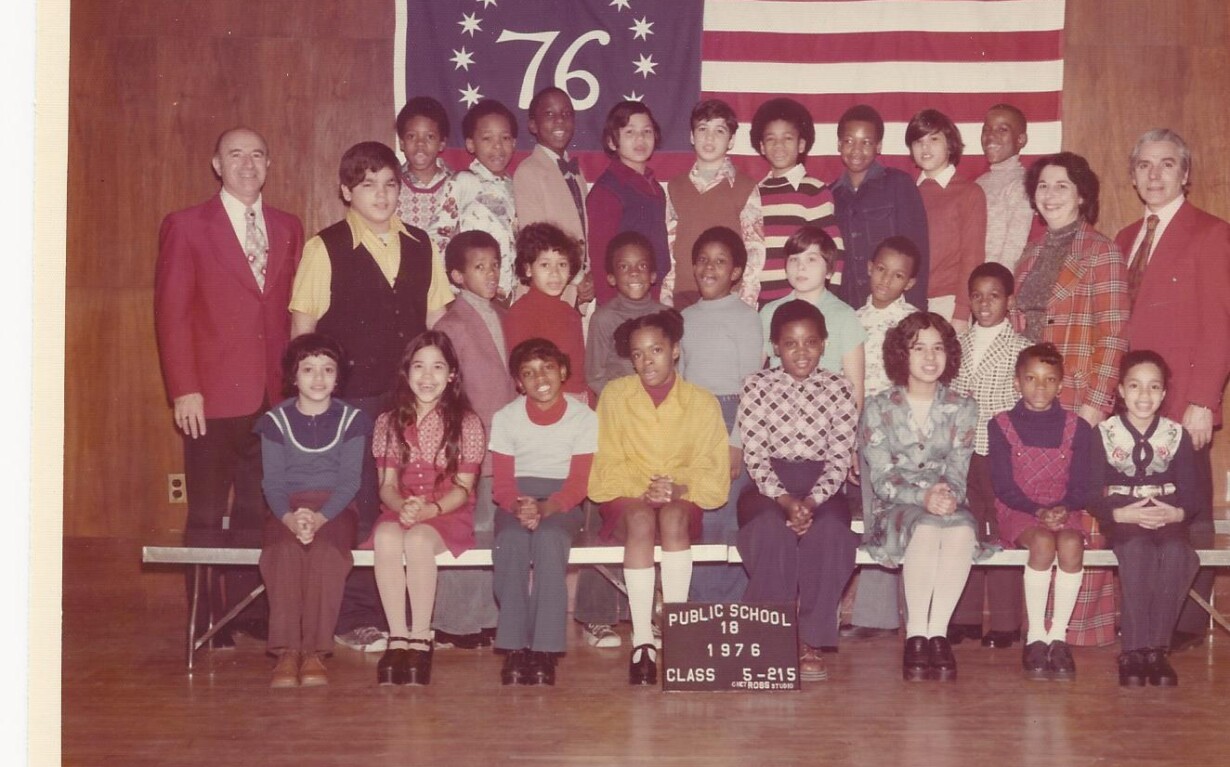 A vintage class photo from 1976 shows a diverse group of students and teachers, embodying early principles of social emotional learning. They pose proudly in the school auditorium before a banner with "76" and stars, alongside a U.S. flag, representing Public School 116, Class 5-8 IS.