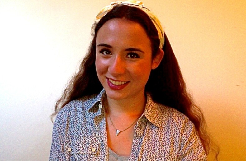 A woman with long, wavy hair smiles at the camera, embodying the positivity of social emotional learning activities. She is wearing a patterned shirt, a necklace, and a headband. The background is a plain, light-colored wall.