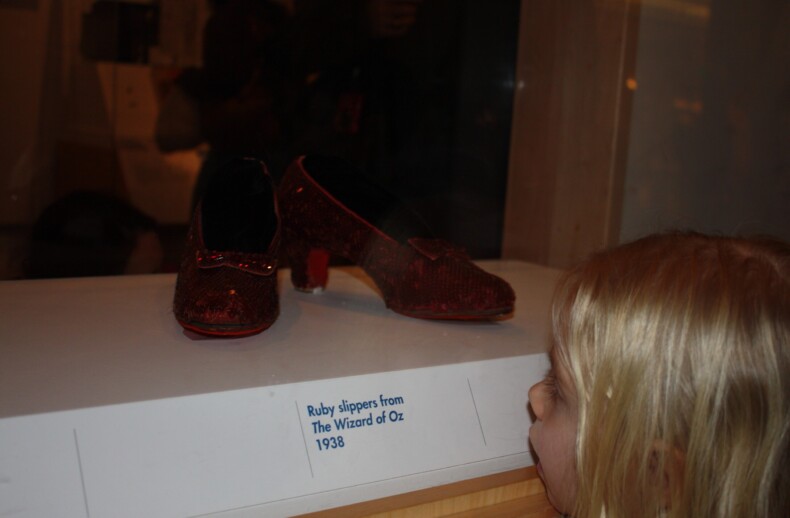 A young girl marvels at a display case containing the iconic ruby slippers from "The Wizard of Oz," 1938. It's a moment that opens doors to SEL activities, fostering curiosity and connection, much like get-to-know-you activities for students in diversity programs.