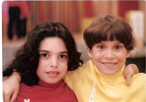 Two children with dark hair and cheerful expressions pose together, embodying the spirit of SEL activities. The child on the left wears a red shirt, while the one on the right sports a yellow shirt. They stand against a colorful, blurred background that highlights their vibrant joy.