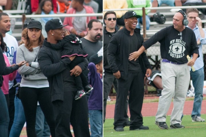 Amidst the vibrant crowd at an outdoor event, a person in a black outfit and cap holds a small child. Nearby, in another moment, they share laughter and shake hands with a man in sports attire and headphones on the field—the scene reminiscent of spirited SEL activities fostering connections.