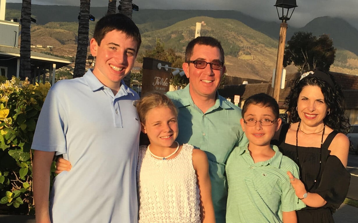 A family of five stands outside, smiling at the camera amid a sunny landscape with hills and trees. The cheerful scene captures a moment that embodies connection, mirroring the essence of activities from social emotional learning curriculums focused on building bonds and understanding.