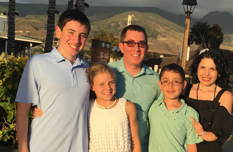 A family of five stands outside, smiling at the camera amid a sunny landscape with hills and trees. The cheerful scene captures a moment that embodies connection, mirroring the essence of activities from social emotional learning curriculums focused on building bonds and understanding.