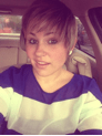 A person with short, styled hair takes a selfie in a car, wearing a blue and white striped shirt and earrings. Their light expression hints at the joy of get to know you activities for students. The softly visible car interior adds to the relaxed mood.