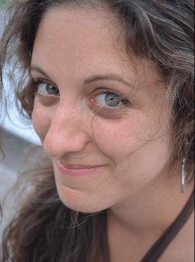 A woman with long, wavy hair smiles softly at the camera. She is wearing earrings and a brown top, subtly reflecting her passion for diversity programs. The background is slightly blurred.