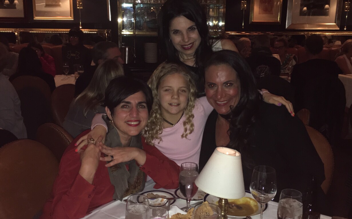 Four people pose happily at a dimly lit restaurant table, engaging in a delightful social emotional learning activity. Surrounded by plates of food and glasses, they enjoy each other's company. Behind them, a warmly decorated interior with framed pictures adds to the cozy atmosphere.