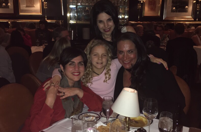 Four people pose happily at a dimly lit restaurant table, engaging in a delightful social emotional learning activity. Surrounded by plates of food and glasses, they enjoy each other's company. Behind them, a warmly decorated interior with framed pictures adds to the cozy atmosphere.