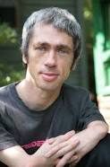 A person with gray hair and a black shirt sits outdoors, embodying the essence of SEL curriculum. The background is blurred greenery; they have a calm expression and are looking at the camera. Their presence channels the tranquility often sought in social emotional learning environments.