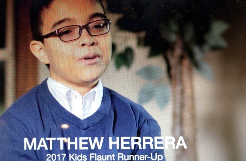 A person wearing glasses and a blue sweater is speaking. Text on the image reads, "MATTHEW HERRERA 2017 Kids Flaunt Runner-Up." In the background, where a blurred plant is visible, elements of social emotional learning activities are subtly suggested.