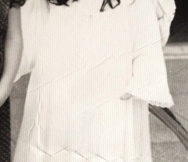 Black and white photo of a young child dressed in a long, flowing costume with a paper crown, embodying the imaginative play often encouraged by SEL activities. They have long hair and are standing indoors with a serious expression. A partial view of another person is visible to the left.