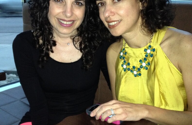 Two women enjoying a meal together at a restaurant. One wears a black top, the other a yellow dress with a beaded necklace. They smile warmly, posing closely with menu and napkin on the table—a picture-perfect moment reflecting the joy of social emotional learning in real life.