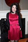 A woman with long dark hair wearing a red satin dress and a black cardigan stands thoughtfully in front of a white fireplace, reflecting the warmth and comfort that SEL activities bring to one's life.