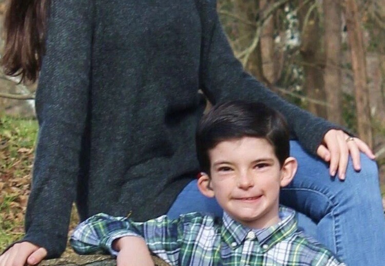 A girl and a young boy smile at the camera while sitting on a stone wall, embodying the spirit of SEL activities. The girl is wearing a dark sweater and jeans, and the boy is in a plaid shirt. The background features trees and foliage, creating an inviting atmosphere for growth and connection.