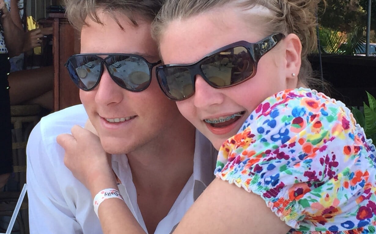 A young woman in a colorful floral top and sunglasses smiles while hugging a man in a white shirt and sunglasses, embodying the warmth of SEL activities. They are outdoors, adding joy to their sunny day, as the man sports a red wristband.