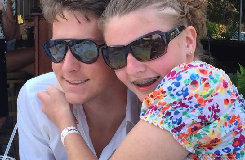 A young woman in a colorful floral top and sunglasses smiles while hugging a man in a white shirt and sunglasses, embodying the warmth of SEL activities. They are outdoors, adding joy to their sunny day, as the man sports a red wristband.