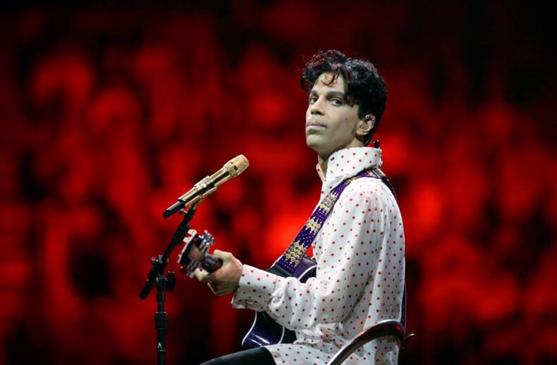 A musician strums his guitar on stage, clad in a white polka-dotted shirt, with a golden microphone before him. The vibrant red backdrop enhances the dramatic atmosphere, mirroring the emotional depth found in social emotional learning curriculum.