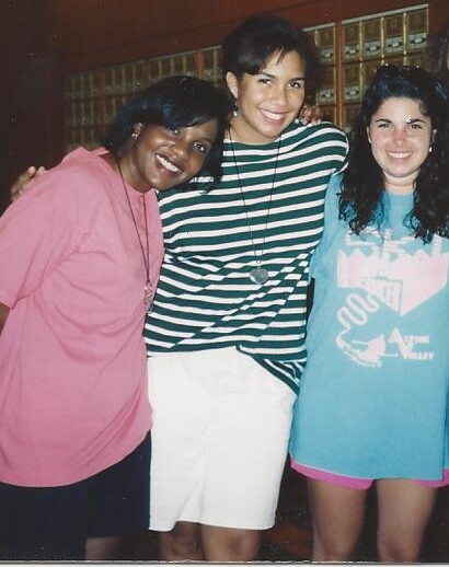 Three people stand close together, smiling at the camera after enjoying some get-to-know-you activities for students. The person on the left wears a pink shirt, the middle sports a green and white striped shirt with white shorts, and the right is in a blue graphic tee paired with pink shorts.