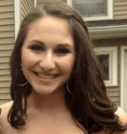 A woman with long brown hair and hoop earrings smiles at the camera, embodying warmth like a well-crafted social emotional learning curriculum. She stands outside in front of a house with brown siding and white-trimmed windows, inviting connection as naturally as get-to-know-you activities for students.