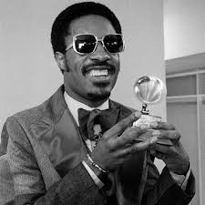 A person wearing sunglasses and a suit, smiling, and holding a Grammy award—showcasing the harmony of self-expression akin to a social emotional learning curriculum. The image is in black and white, capturing timeless confidence.
