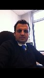 A person wearing a dark sweater over a collared shirt and blue tie is seated in an office chair. They are inside an office focused on diversity programs, with a window in the background letting in light, fostering an atmosphere conducive to social emotional learning activities.