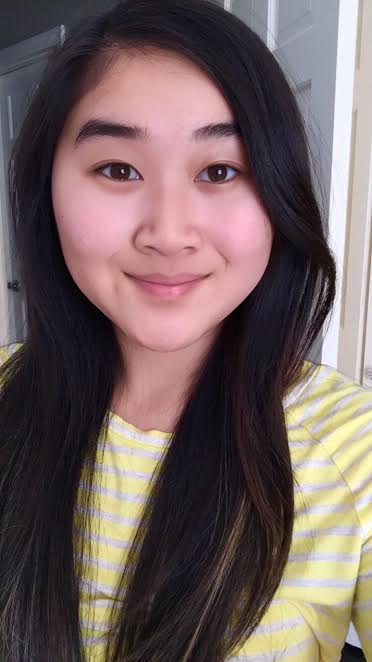A person with long dark hair and a pleasant smile is wearing a yellow striped shirt, ready to engage in get-to-know-you activities for students. The background shows a white doorway.