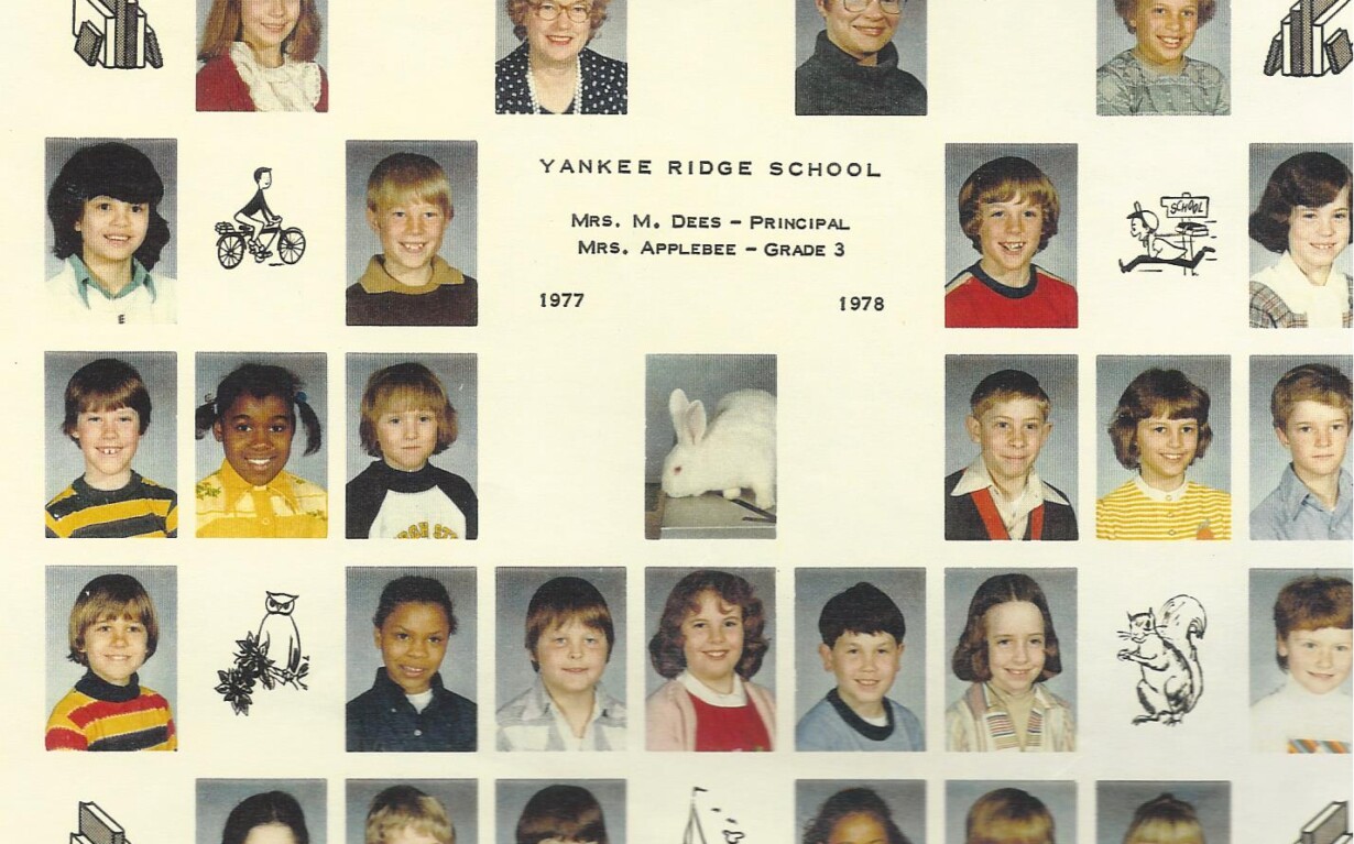 A class photo collage titled "Yankee Ridge School" showcases individual portraits of children and teachers from the year 1977-1978. Enhanced with whimsical drawings of a bicycle, a rabbit, a cat, and a church, it subtly hints at early diversity programs through its charming array of personalities.