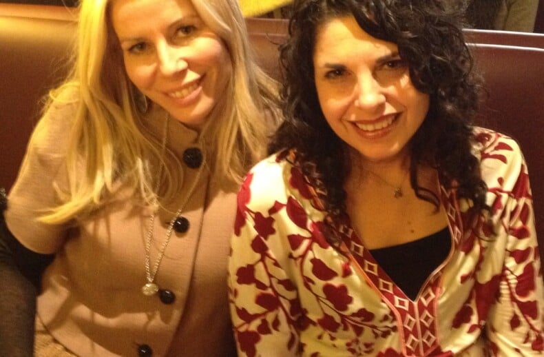 Two women, engaging in a delightful moment of social emotional learning activities, sit together in a cafe booth, smiling at the camera. The woman on the left flaunts long blonde hair, while her friend boasts curly dark hair. A white cup rests invitingly on the table before them.