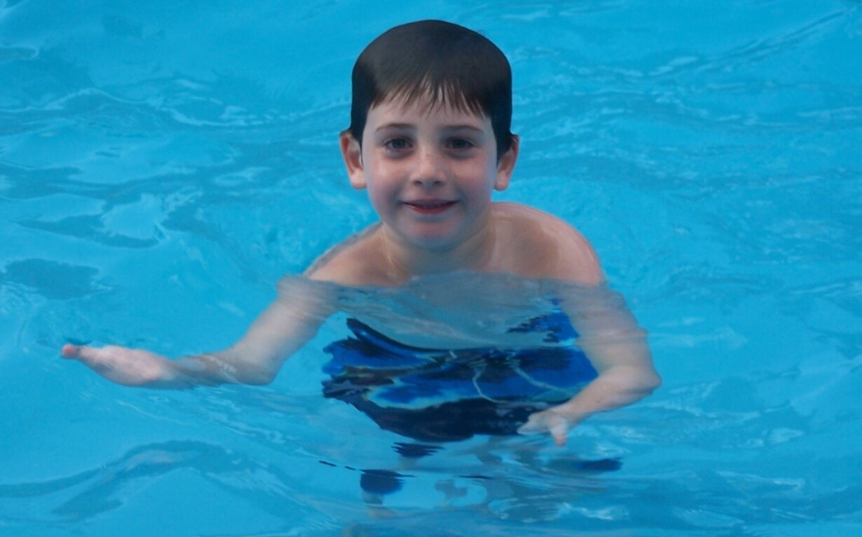 A young boy in a blue swimsuit smiles while swimming in a pool, surrounded by clear blue water, embracing the joy and inclusion found in SEL activities.