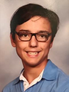 A young person with short dark hair and glasses smiles softly at the camera, embodying the spirit of a modern SEL curriculum. They are wearing a blue collared shirt over a white undershirt against a neutral background.