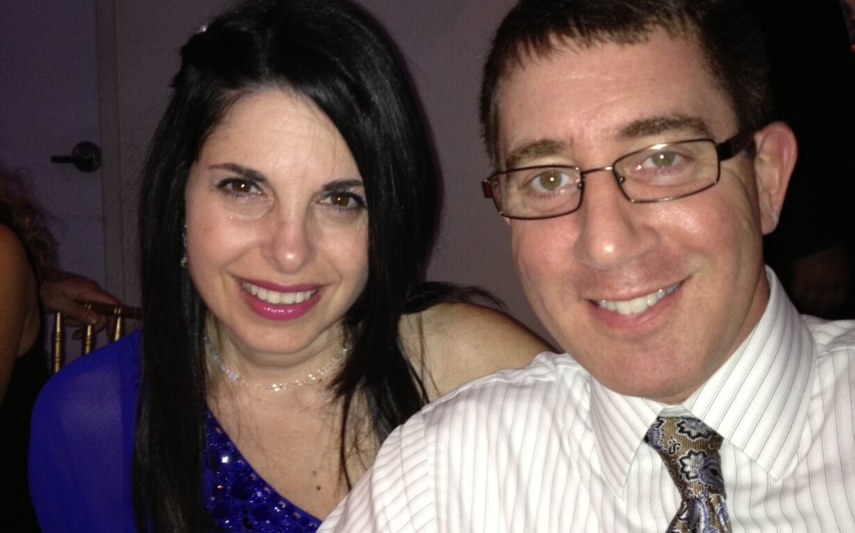 At a formal event, a smiling couple sits closely. The woman, in a blue dress with long dark hair, complements the man in glasses sporting a striped shirt and paisley tie. In the backdrop of chandeliers, their connection mirrors lessons from an SEL curriculum on building meaningful relationships.