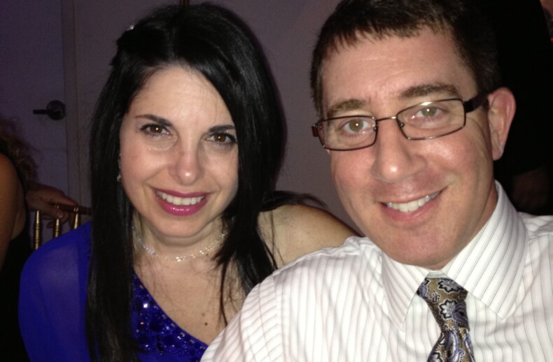 At a formal event, a smiling couple sits closely. The woman, in a blue dress with long dark hair, complements the man in glasses sporting a striped shirt and paisley tie. In the backdrop of chandeliers, their connection mirrors lessons from an SEL curriculum on building meaningful relationships.
