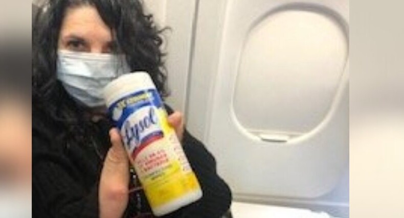 A person wearing a face mask holds a container of disinfecting wipes, sitting by an airplane window, reflecting on the insights gained from their recent SEL curriculum training.