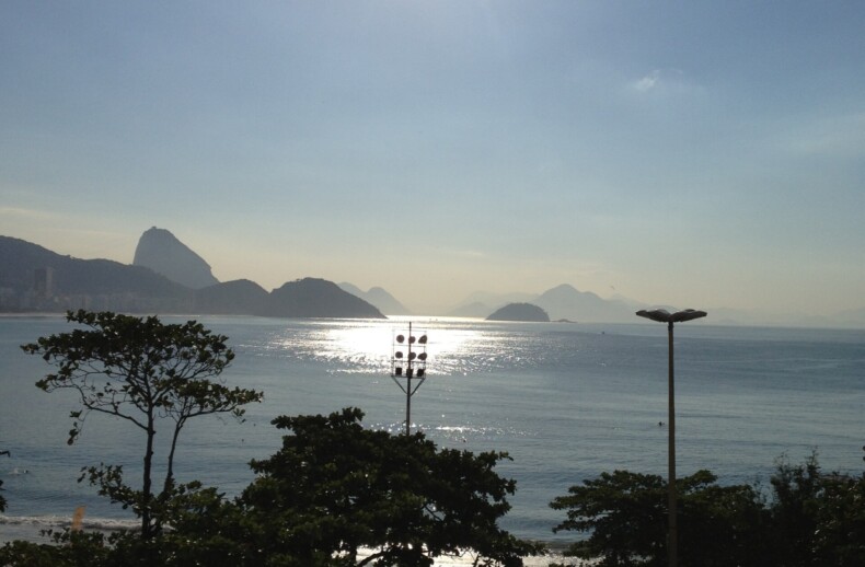 Bright sun over a peaceful beach with trees and distant mountains, mirroring the harmonious blend of a SEL curriculum. The sunlight reflects on the calm sea, creating a serene atmosphere akin to get-to-know-you activities for students fostering genuine connections.