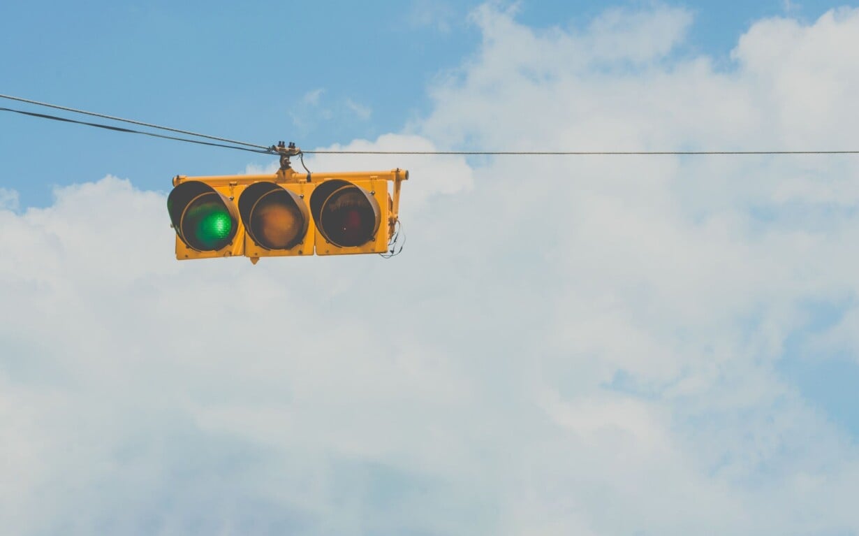 A traffic light hangs on a wire against a bright blue sky with clouds. The green light is illuminated, like a signal for diversity programs to proceed. As the yellow and red lights stay off, it's a reminder of progress and the harmonious flow we strive for in community growth.